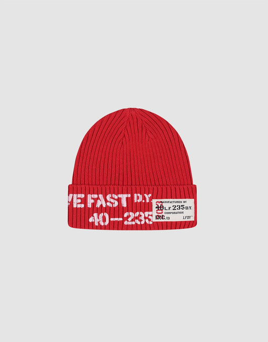 The LIVE FAST DIE YOUNG Live Fast Army Beanie is a red, 100% cotton ribbed knit hat featuring white text and a rectangular patch with black and red designs, numbers, and "Live Fast" print on the front. Plain light gray background.
