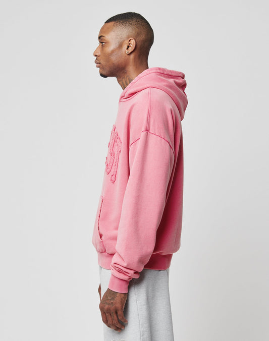 A man stands in profile facing left, wearing the LIVE FAST DIE YOUNG Ripped College Hooded sweatshirt in pink with an oversize fit and light gray pants against a plain light background.