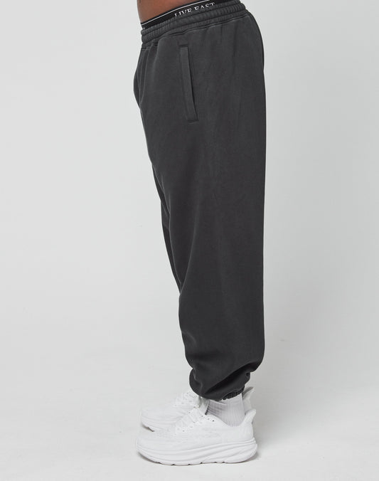 A person stands sideways wearing LIVE FAST DIE YOUNGs LFDY Sphere Jogger in black, paired with white socks and sneakers, set against a plain white background.
