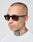 A man with a shaved head and neck tattoos wears LIVE FAST DIE YOUNG LFDY x Chimi Shades 03 and a white t-shirt, looking slightly to the side against a plain, light background.