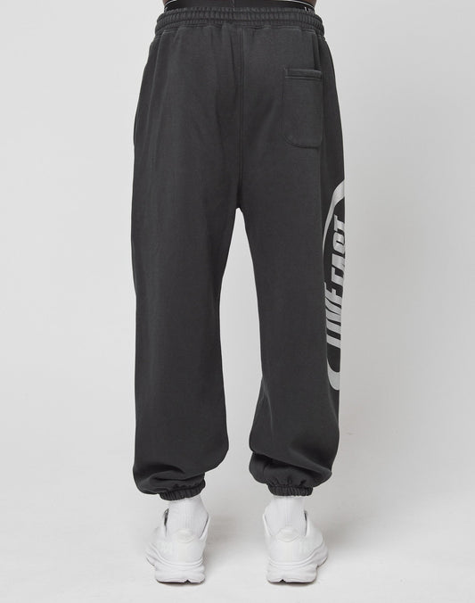 A person wears black LFDY Sphere Jogger pants by LIVE FAST DIE YOUNG, featuring a back pocket, Oversize Fit, and distinctive side logo, paired with white sneakers, standing against a plain white background.