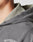 Close-up of a persons neck and shoulder wearing the LFDY Cross Hooded Zip by LIVE FAST DIE YOUNG, featuring LIVE FAST text, layered over a textured light collared shirt. Background is plain and out of focus.