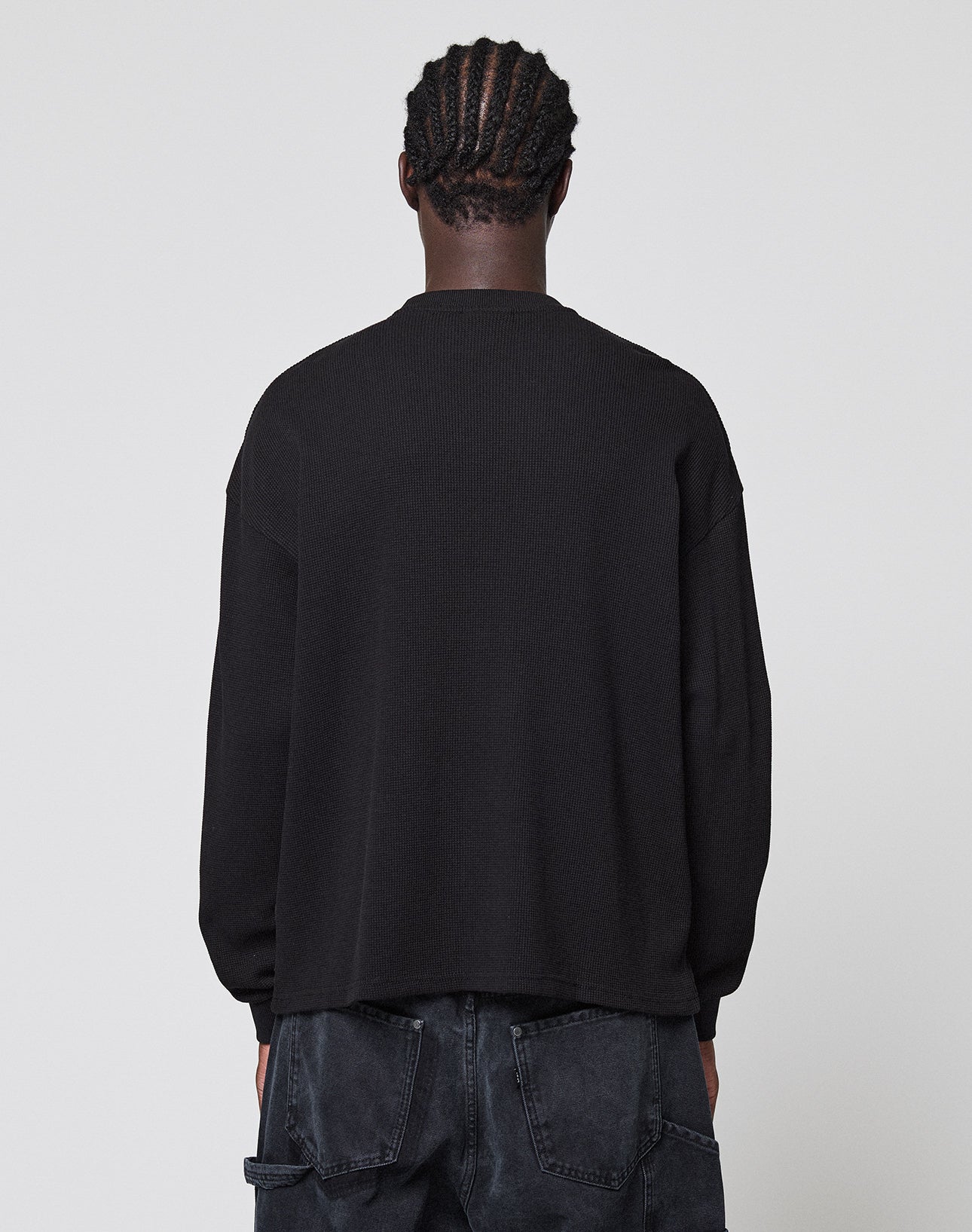 A person with braided hair, seen from behind, wears the LIVE FAST DIE YOUNG Blank Waffle Longsleeve in black and dark denim jeans against a plain light gray background.