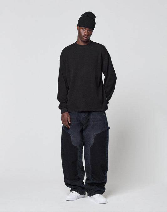 A person wears a black Blank Waffle Longsleeve by LIVE FAST DIE YOUNG with Ripp-Bündchen and Oversize Fit, loose dark jeans with light patches, and white sneakers, standing relaxed against a plain white background.