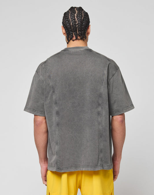 A person with braided hair is seen from the back, wearing the LIVE FAST DIE YOUNG Live Fast Wave Tee in faded gray with an oversize fit, paired with bright yellow shorts, standing against a plain light gray background.