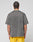 A person with braided hair is seen from the back, wearing the LIVE FAST DIE YOUNG Live Fast Wave Tee in faded gray with an oversize fit, paired with bright yellow shorts, standing against a plain light gray background.