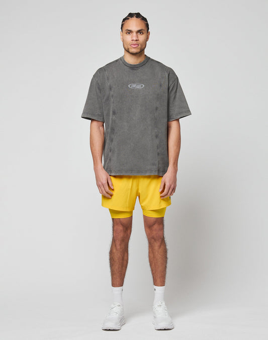 A man faces forward against a plain background, wearing the LIVE FAST DIE YOUNG Live Fast Wave Tee in gray with a reflective front print, bright yellow shorts, white socks, and white sneakers. His hands rest loosely by his sides.