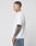 A man with short hair and tattoos on his neck and arm stands in profile wearing the LFDY Triple Racing Tee by LIVE FAST DIE YOUNG—an oversize fit white T-shirt with multilogo frontprint, made from 100% Baumwolle, paired with blue jeans against a gray background.