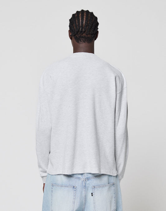 A person with braided hair faces away from the camera, wearing a LIVE FAST DIE YOUNG Blank Waffle Longsleeve in light gray Oversize Fit and light blue jeans against a plain white background.