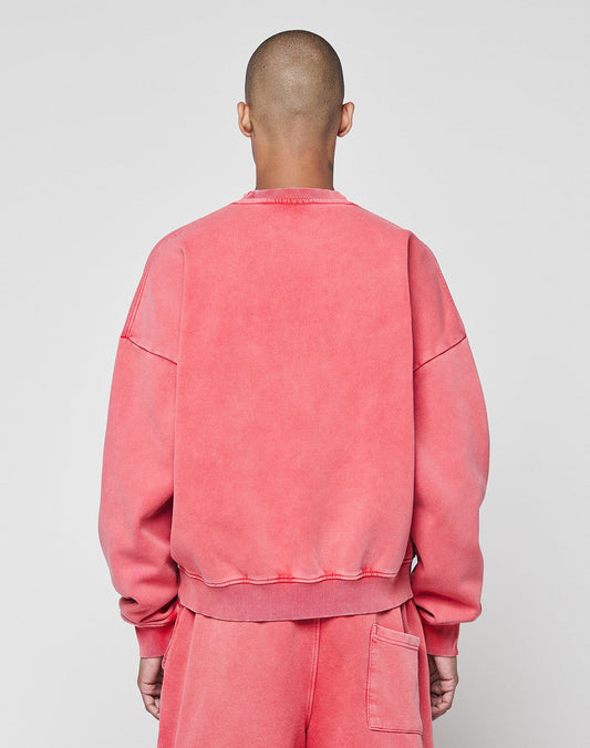A person with a shaved head faces away from the camera, wearing the oversize Basic LiveFast Sweater and matching sweatpants by LIVE FAST DIE YOUNG in faded pink, set against a plain light gray background.