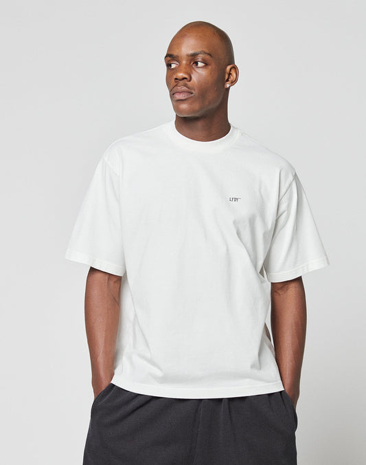 A person wears the LFDY Zizou Tee by LIVE FAST DIE YOUNG—an oversize white 100% Baumwolle T-shirt with small LFDY chest text—and black pants, standing against a plain light gray background looking to the side.