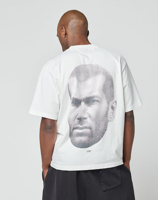 Wearing an oversize fit LFDY Zizou Tee by LIVE FAST DIE YOUNG, featuring 100% cotton and a bold black-and-white close-up portrait as a backprint, the person stands against a plain light background.