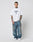 A man with short hair and tattoos wears the LFDY Triple Racing Tee by LIVE FAST DIE YOUNG, an oversized white T-shirt styled with baggy blue jeans and white sneakers, posing against a plain light background.