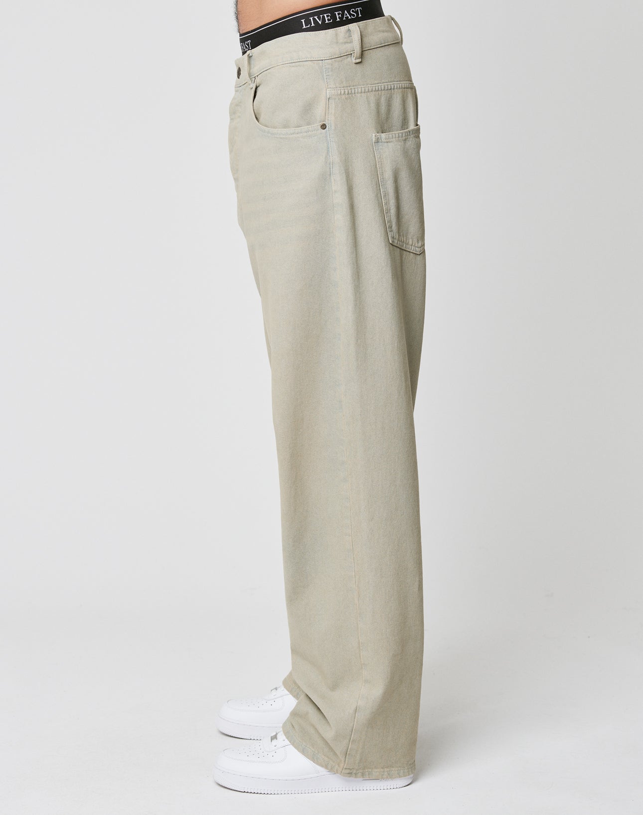 A person in LFDY Baggy Denim by LIVE FAST DIE YOUNG, white sneakers, and black underwear with LIVE FAST on the waistband stands in profile against a plain white background.