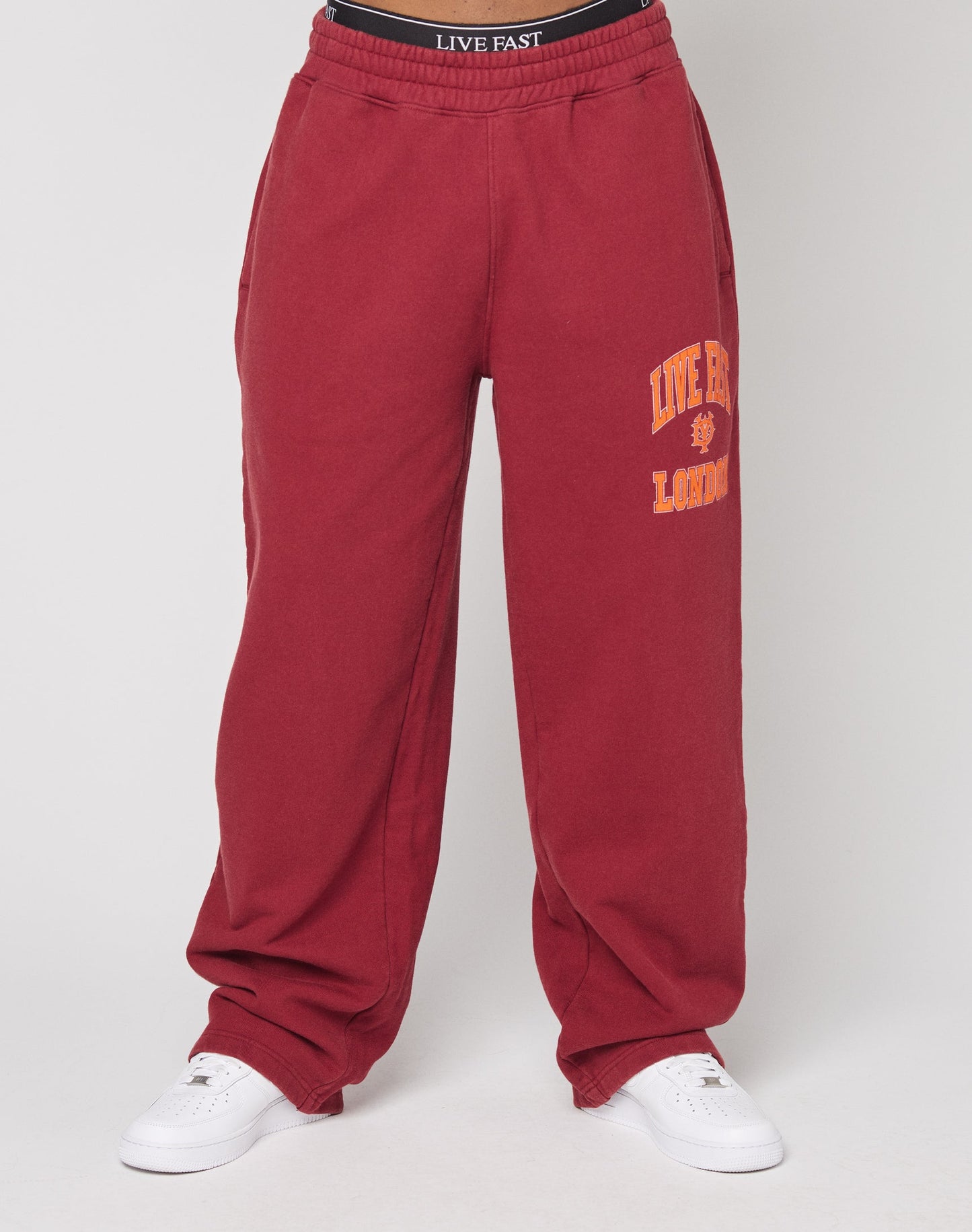 Model wears the Live Fast London Wide Jogger by LIVE FAST DIE YOUNG—red, wide fit, cotton sweatpants with yellow LIVE FAST LONDON on the left thigh and elastic waistband with LIVE FAST text. Styled with white sneakers against a plain background.