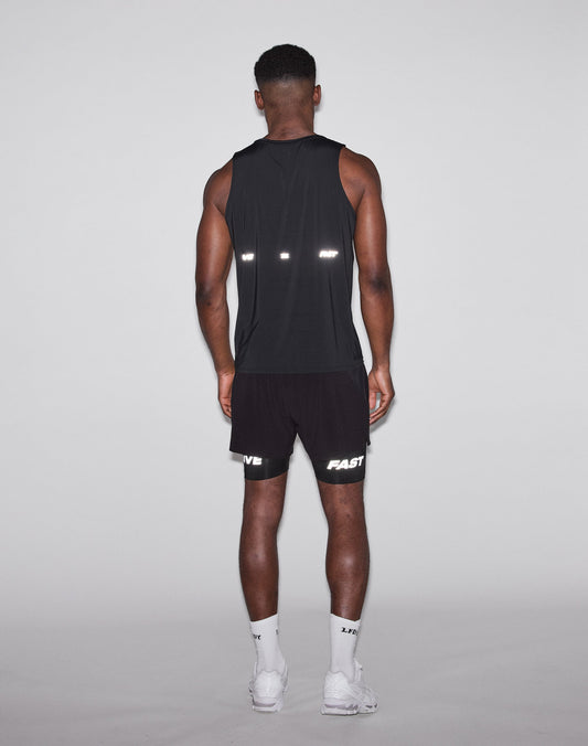 A man faces away from the camera, wearing a black LIVE FAST DIE YOUNG Live Fast Performance Tank, black shorts with FAST and LIVE in reflective print, white socks, and white sneakers against a plain light background.