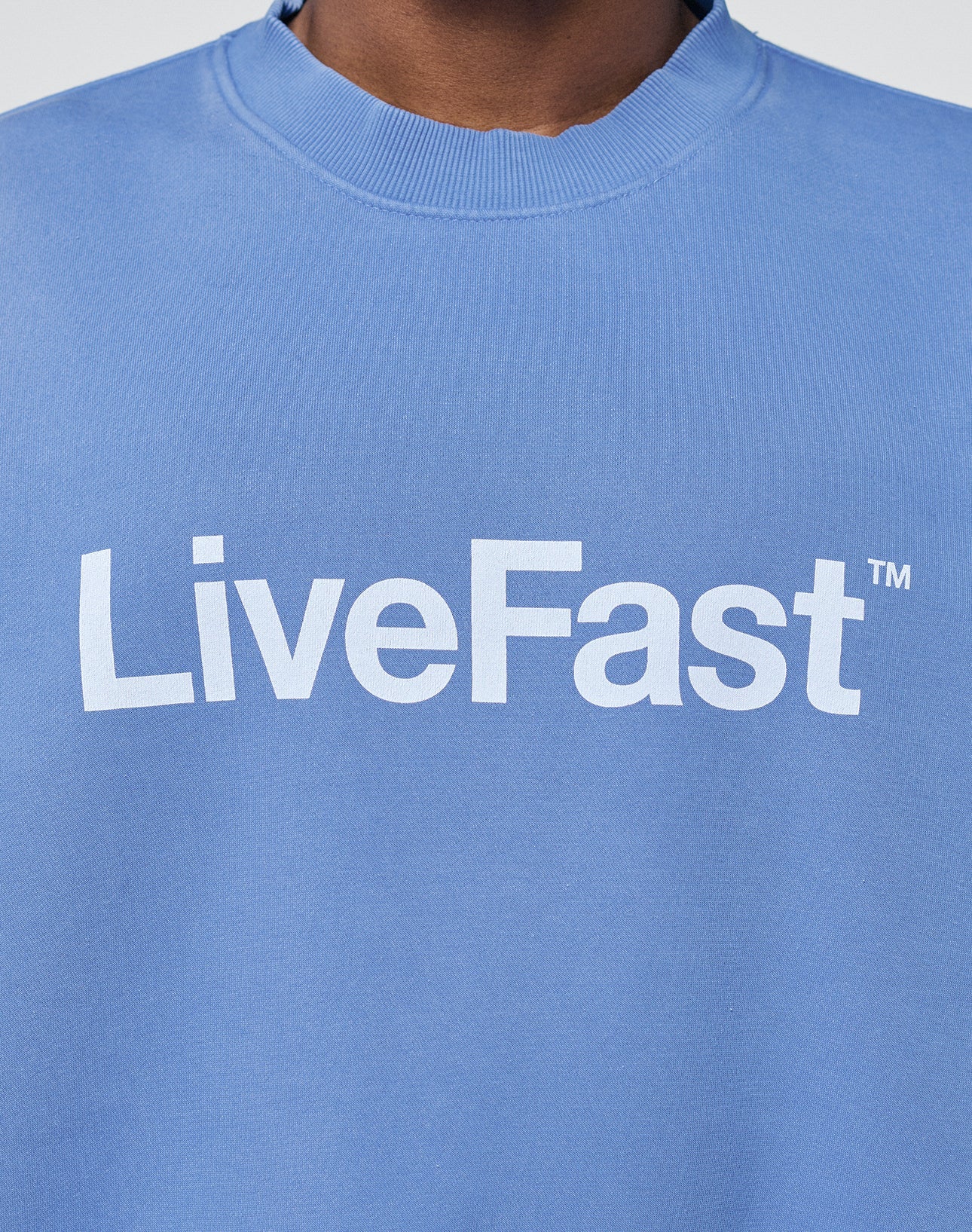 A person wears the Basic LiveFast Sweater by LIVE FAST DIE YOUNG, featuring an Oversize Fit, subtle Faded Look, and bold white LiveFast™ print across the chest.