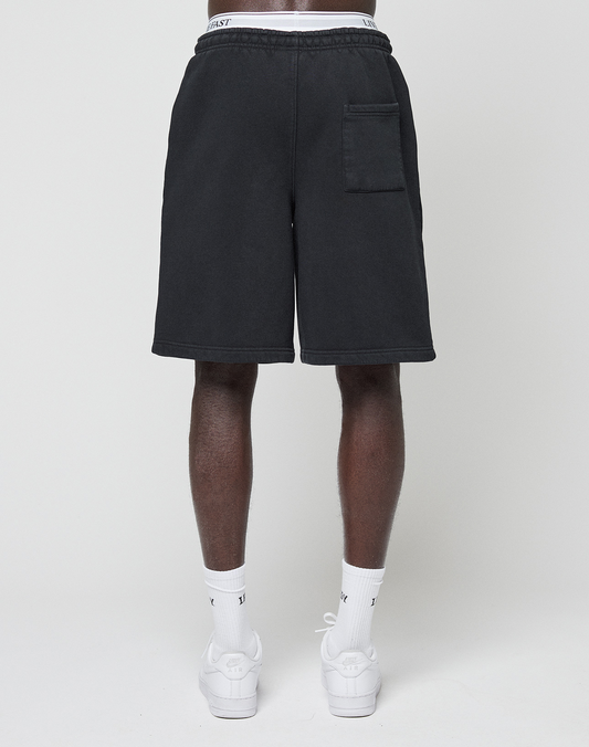 A person stands facing away from the camera wearing LIVE FAST DIE YOUNG Basic Shorts with an elastic waistband, single right back pocket, white socks, and white sneakers against a plain light background.