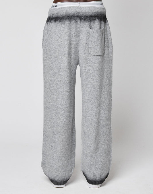 LIVE FAST DIE YOUNG’s Live Fast Boucle Pants feature a wide fit, straight leg, single front pocket, elastic waistband with text, and a gradient from dark to light gray at the waist and ankles. Displayed on a plain background.