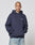 A person with a shaved head and face tattoos wears the Live Fast Plain Hooded by LIVE FAST DIE YOUNG, an oversize fit navy hoodie with "LIVIN FAST" front print, paired with light blue jeans, posing hands-in-pocket against a plain light background.