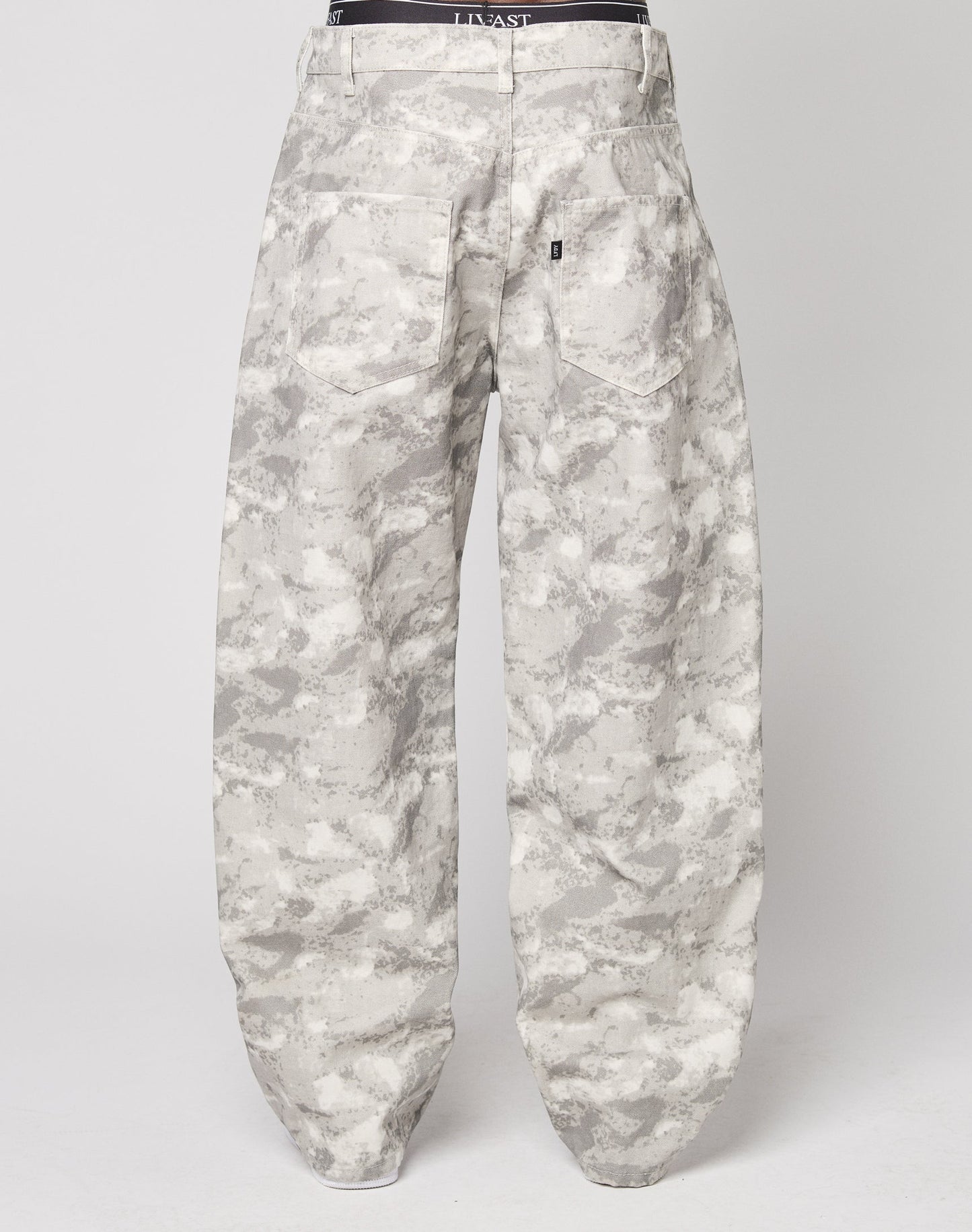 The LIVE FAST DIE YOUNG Live Fast Canvas Pants are baggy, high-waisted, and made from 100% Baumwolle. They feature a light grey and white camo print, straight legs, two large back pockets, and a black waistband. Shown from the back.