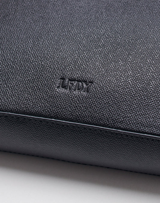 Close-up of a textured black Rindsleder surface on the LIVE FAST DIE YOUNG Airliner Bag, featuring an embossed TUDY logo at the center. The image highlights the detailed grain and elegant embossed finish.