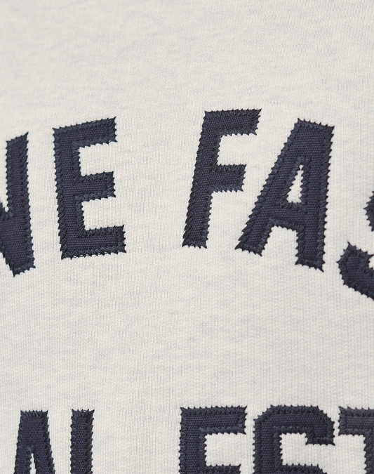 Close-up of white 100% cotton LFDY Heavyweight Lounge Sweater by LIVE FAST DIE YOUNG, featuring large dark blue embroidered letters. Only parts of words, such as "NE FAS," are visible on the fabric.