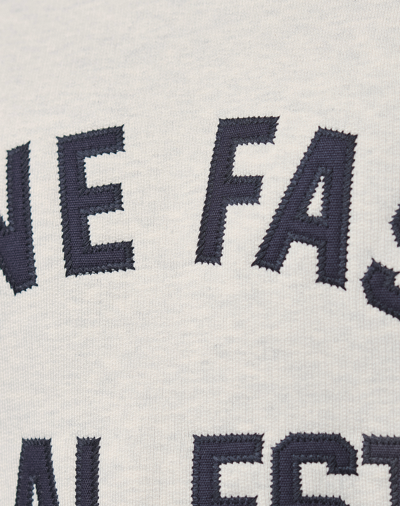 Close-up of white 100% cotton LFDY Heavyweight Lounge Sweater by LIVE FAST DIE YOUNG, featuring large dark blue embroidered letters. Only parts of words, such as "NE FAS," are visible on the fabric.