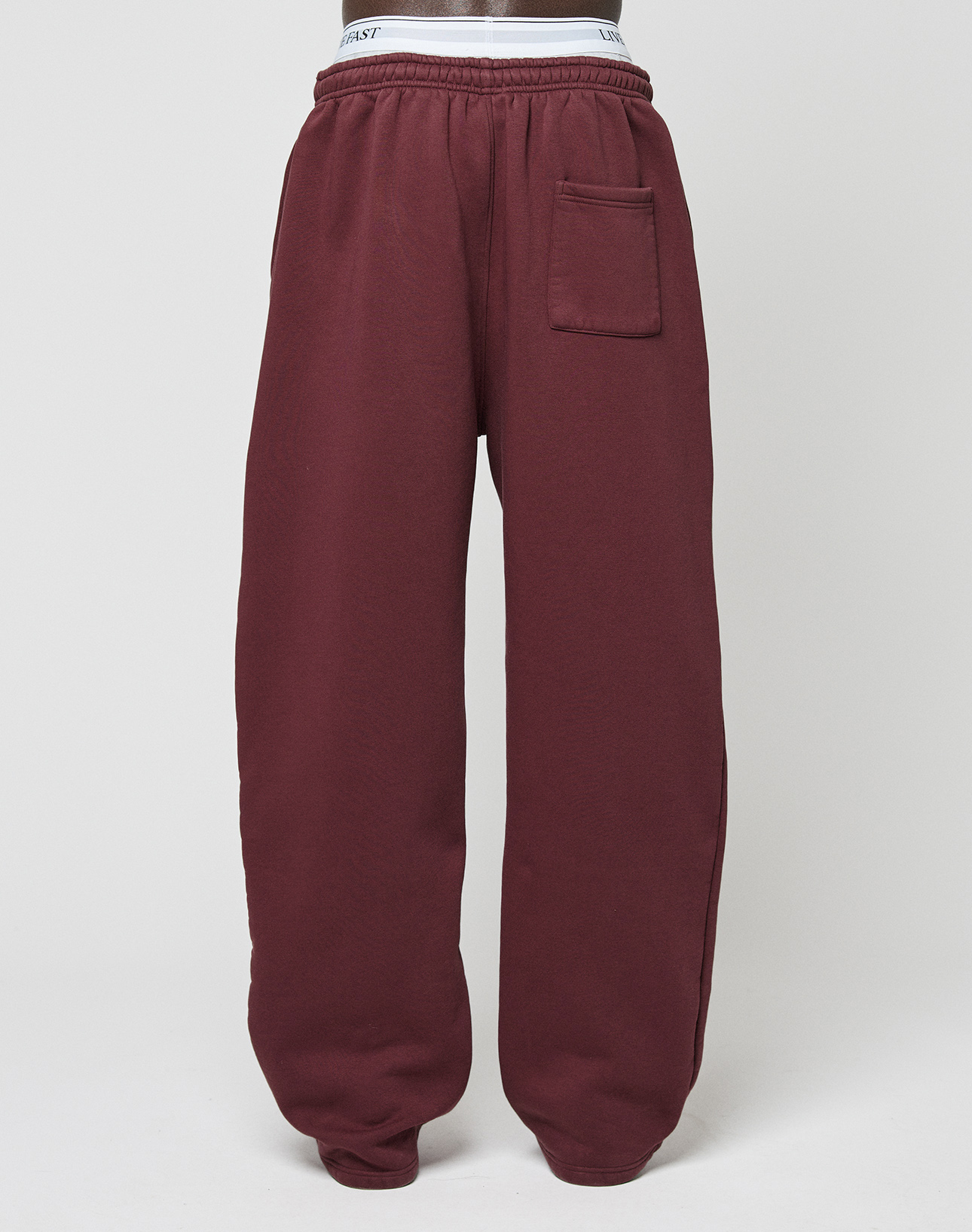 The Basic Wide Jogger by LIVE FAST DIE YOUNG features a maroon wide fit, elastic waistband and cuffs, logo print, and a right-side patch pocket, shown against a plain white background.
