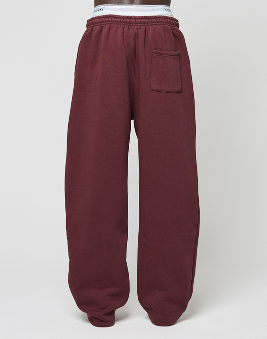 The Basic Wide Jogger by LIVE FAST DIE YOUNG features a maroon wide fit, elastic waistband and cuffs, logo print, and a right-side patch pocket, shown against a plain white background.