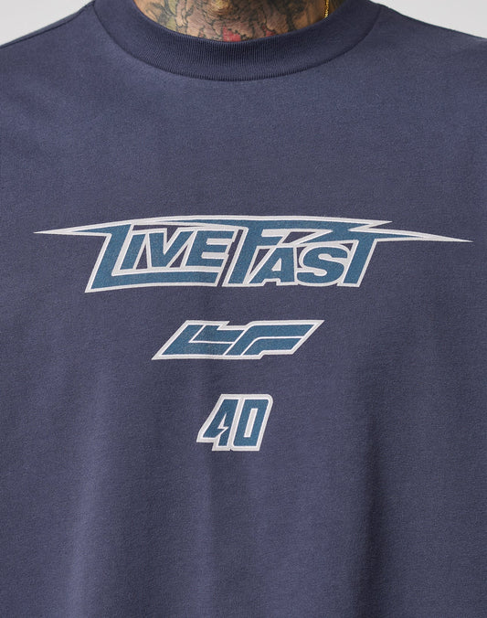 The LFDY Triple Racing Tee by LIVE FAST DIE YOUNG is a navy oversize t-shirt with “LIVE FAST” in stylized white and blue, LF and 40 below, plus multilogo frontprint. Made of 100% cotton. A tattooed neck appears at the image top.