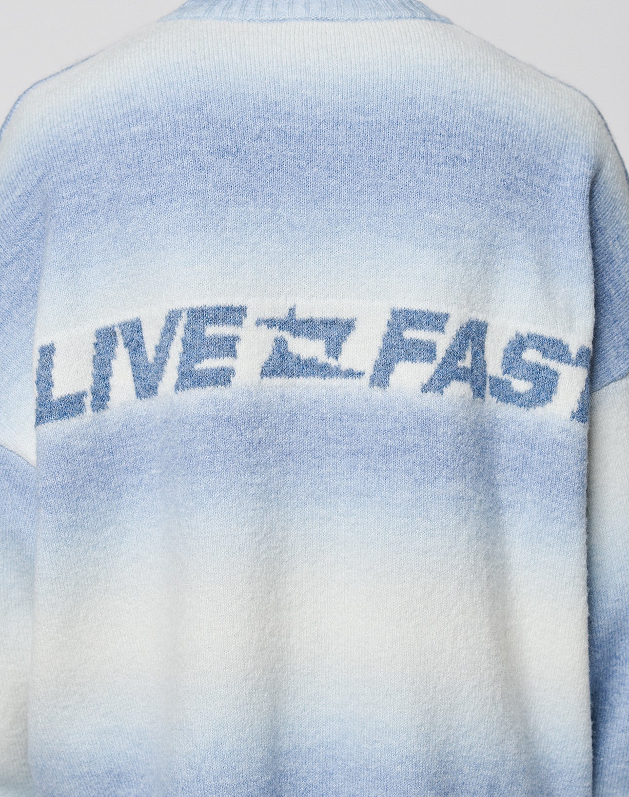 Back view of the Live Fast Boucle Sweater by LIVE FAST DIE YOUNG, featuring a gradient blue and white pattern, bold "LIVE FAST" text split by a speeding car graphic, and angestrickte Bündchen for unique detail.