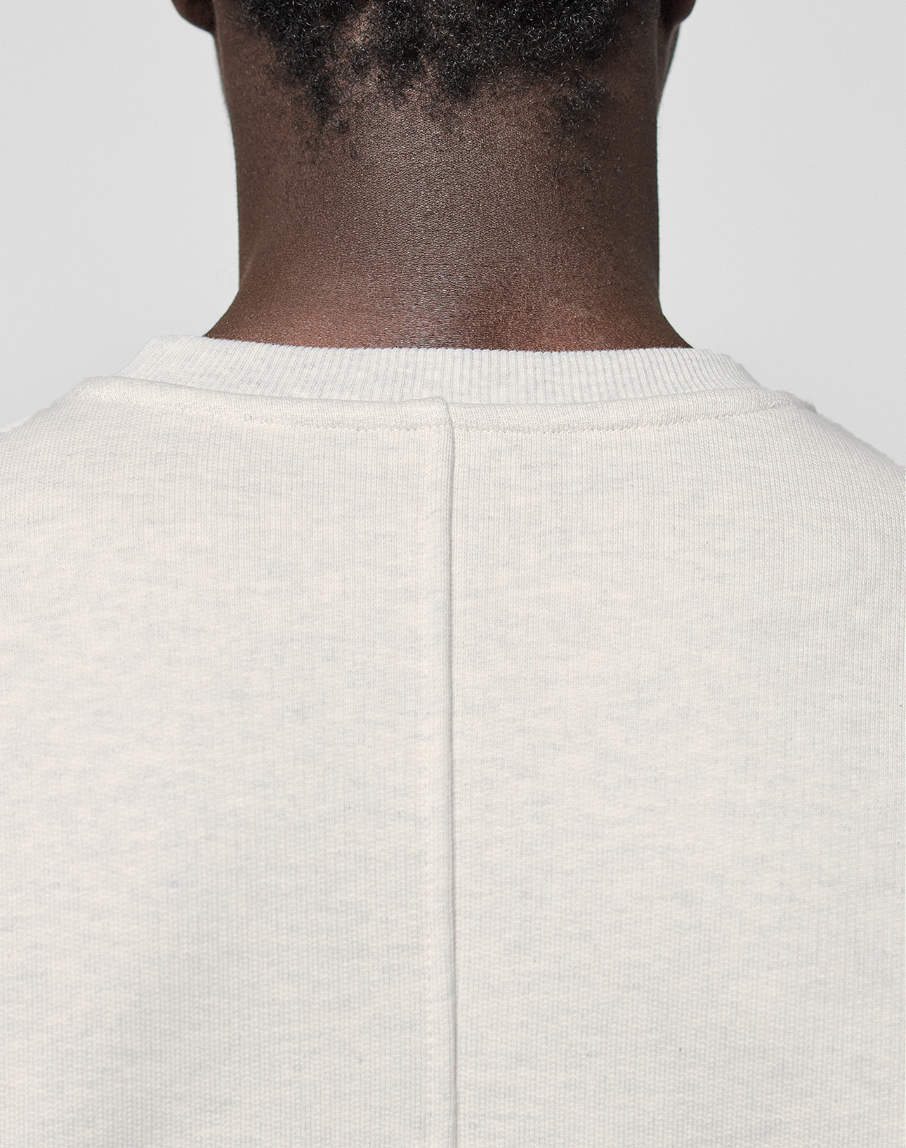 Close-up of the back of a person's neck and shoulders, wearing the LIVE FAST DIE YOUNG LFDY Heavyweight Lounge Sweater. This light-colored, textured oversize crewneck features a central seam and is crafted from 100% Baumwolle for comfort and durability.