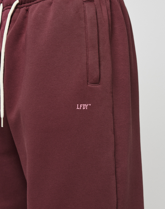 Close-up of a person wearing the LIVE FAST DIE YOUNG Basic Wide Jogger in maroon with wide fit, side pockets, white drawstrings, and small white LFDY™ logo embroidered on the left thigh.