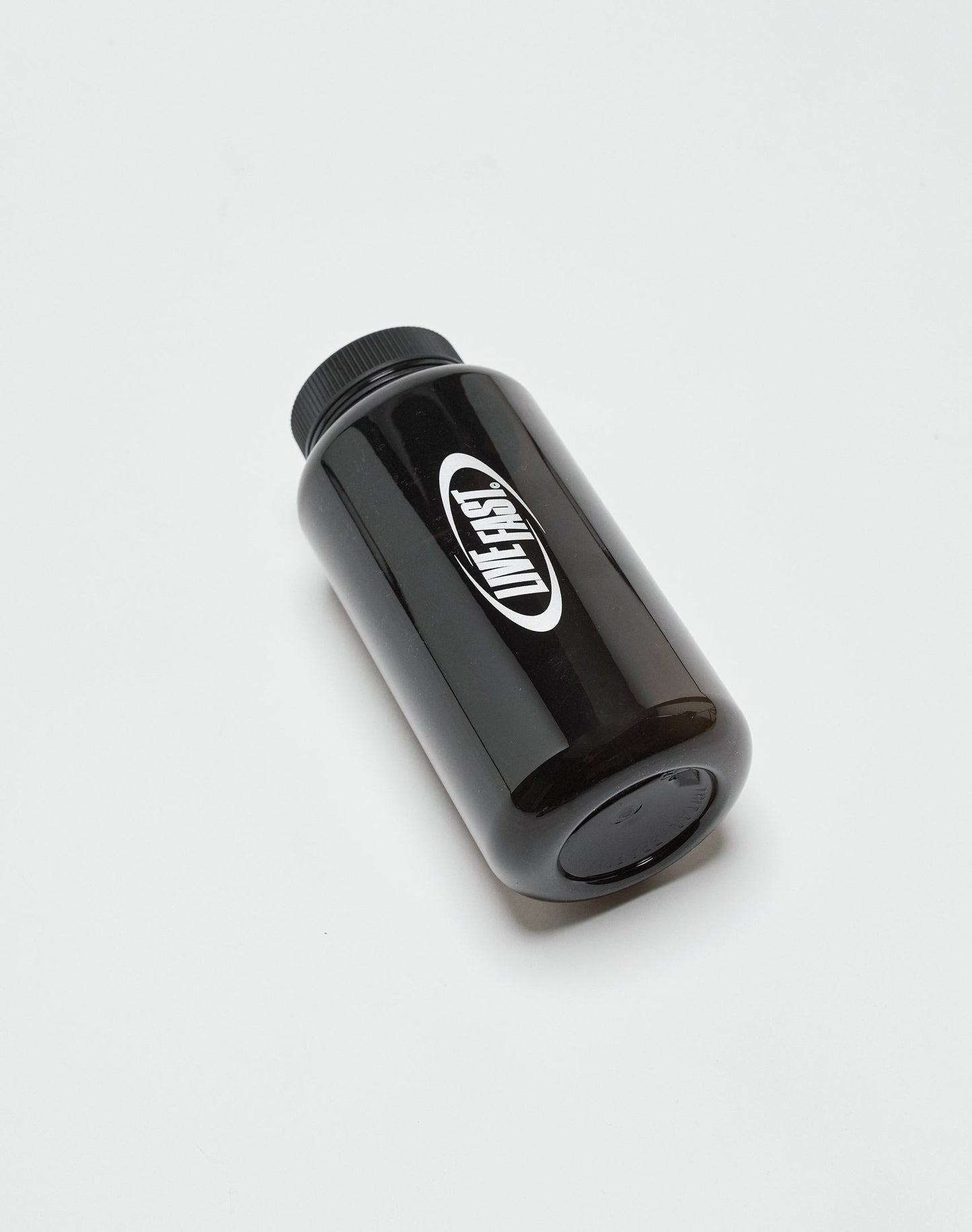 A black plastic Live Fast Performance Gym Bottle from LIVE FAST DIE YOUNG, featuring a black screw cap, lies on its side on a white surface. The BPA-free bottle has a white oval label with bold black branding.| plain