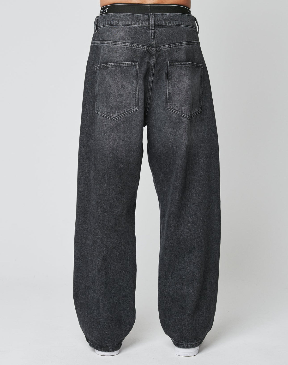 Someone is shown from the back wearing the LFDY Baggy Denim by LIVE FAST DIE YOUNG—baggy fit, dark gray jeans with two large back pockets, a slightly faded look, and wide straight legs, all set against a plain white background.