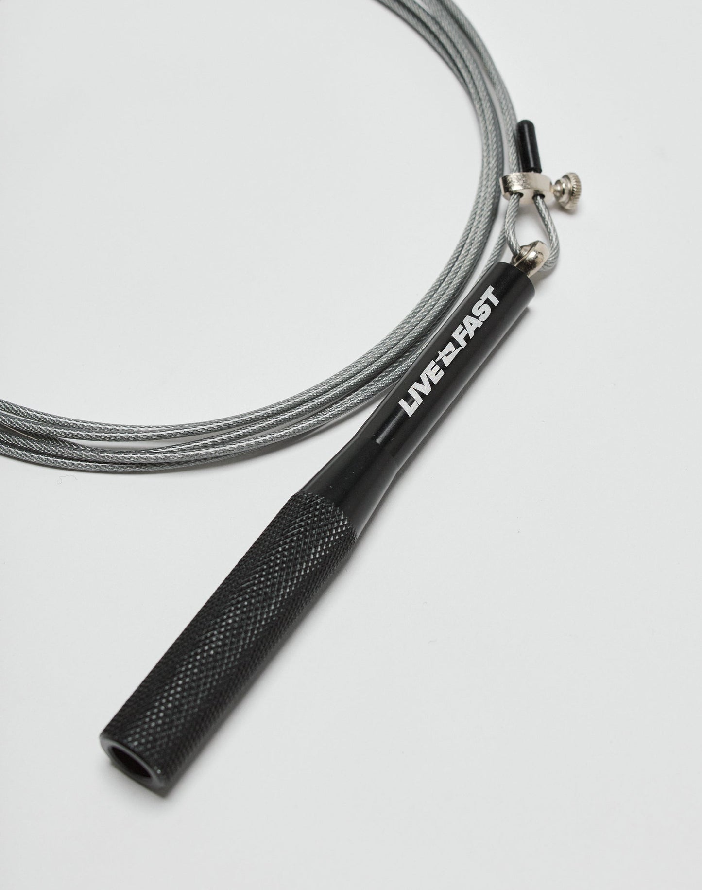 The Live Fast Performance Jump Rope by LIVE FAST DIE YOUNG features a black handle with LIVE•FAST in white and an adjustable wire cable, shown on a white surface.