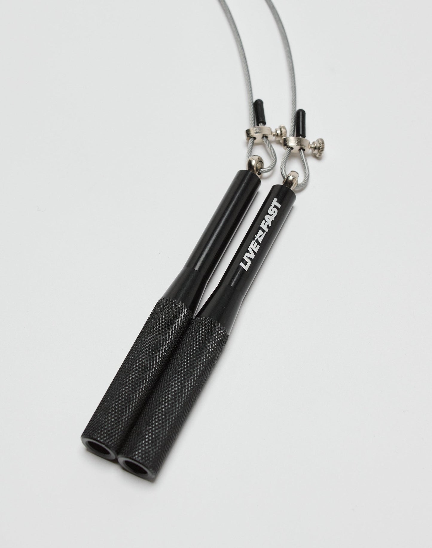 A close-up of the LIVE FAST DIE YOUNG Live Fast Performance Jump Rope, featuring black textured metal handles with LIVE FAST on one side, and an adjustable wire cable secured with metal screws, all on a white background.