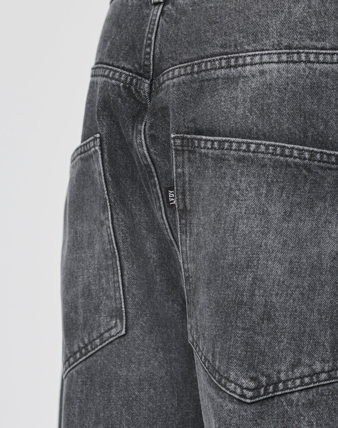 Close-up of the back pocket of LFDY Baggy Denim by LIVE FAST DIE YOUNG, featuring black washed denim, detailed stitching, a small black tag with white text, baggy fit, and made from 100% Baumwolle.