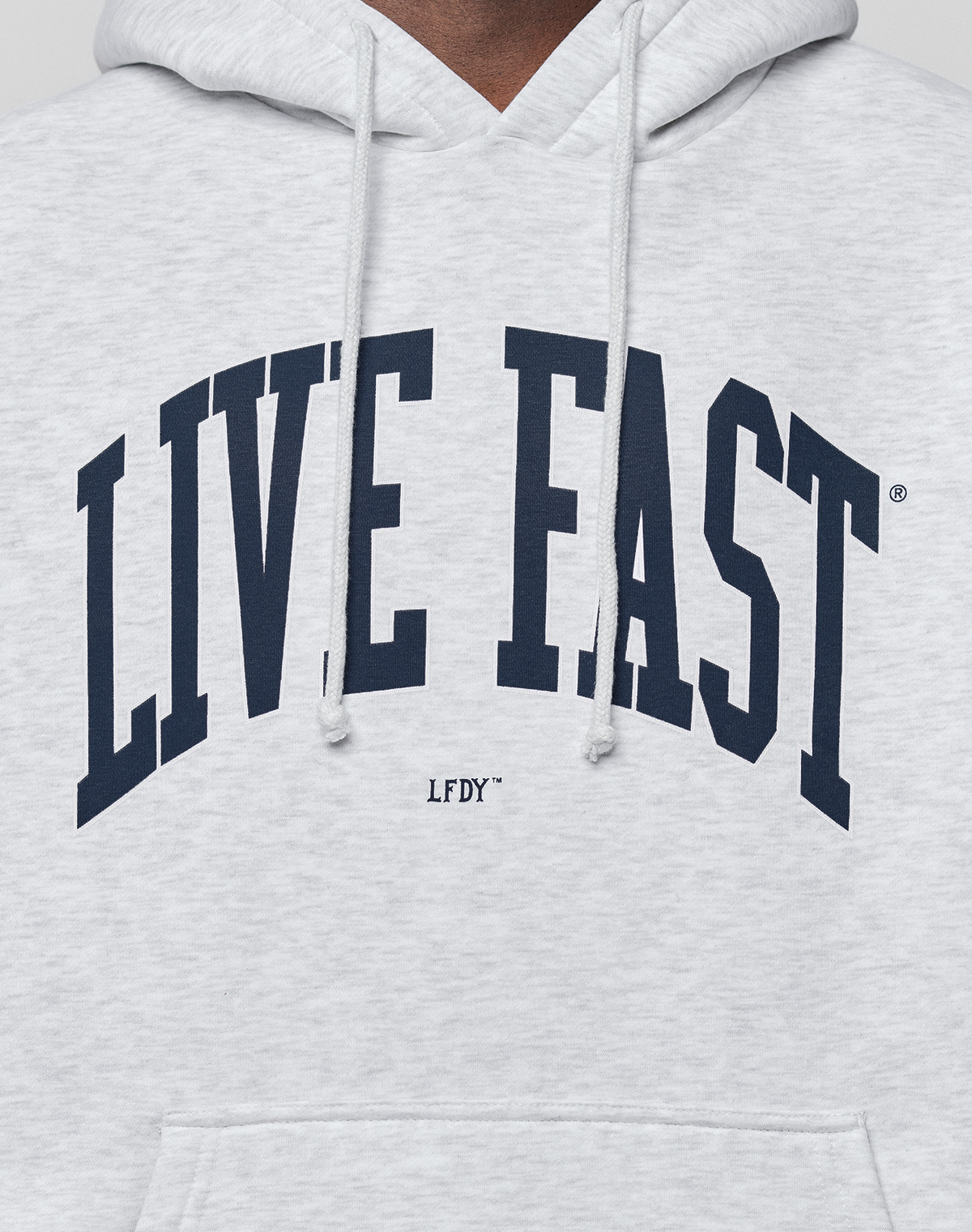 A close-up of the LIVE FAST DIE YOUNG Live Fast College Hooded, an oversized light gray hoodie in soft cotton, with bold navy "LIVE FAST" front print, smaller "LFDY" underneath, and visible drawstrings.