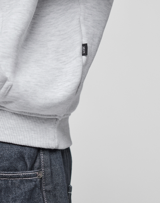 Close-up of a person wearing the LIVE FAST DIE YOUNG Live Fast College Hooded in light gray paired with blue jeans. Only the lower part of the hoodie and the jeans' waistband are visible.