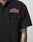 A person wears the black LFDY Workwear Shirt by LIVE FAST DIE YOUNG, featuring a vintage wash, chest pocket with branded patch, and relaxed oversize fit. Tattoos on their arm and neck enhance the laid-back style.