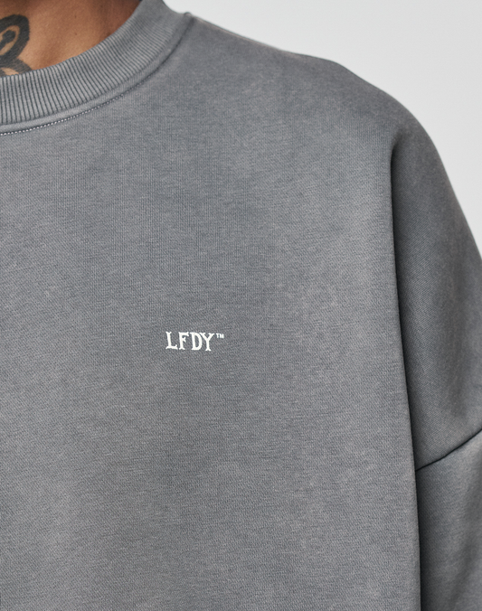 Close-up of a person wearing the Basic Chest Sweater by LIVE FAST DIE YOUNG in Oversize Fit, featuring a small white LFDY™ front print on the chest. Part of the neck and a tattoo appear at the top left.
