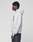 A person with short curly hair stands in profile, wearing a LIVE FAST DIE YOUNG Live Fast College Hooded sweatshirt in light gray with front pocket and dark jeans, set against a plain light gray background.