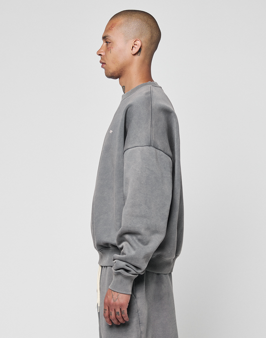 A person with a shaved head is shown in profile, wearing the LIVE FAST DIE YOUNG Basic Chest Sweater in gray and matching pants, styled in an oversize fit, against a plain white background.