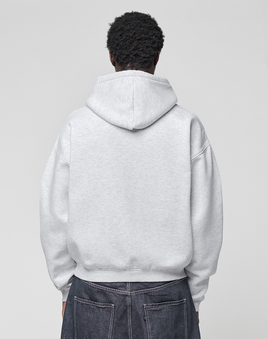 A person faces away from the camera, wearing a LIVE FAST DIE YOUNG Live Fast College Hooded oversize light gray sweatshirt and dark denim jeans against a plain light background.