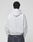A person faces away from the camera, wearing a LIVE FAST DIE YOUNG Live Fast College Hooded oversize light gray sweatshirt and dark denim jeans against a plain light background.