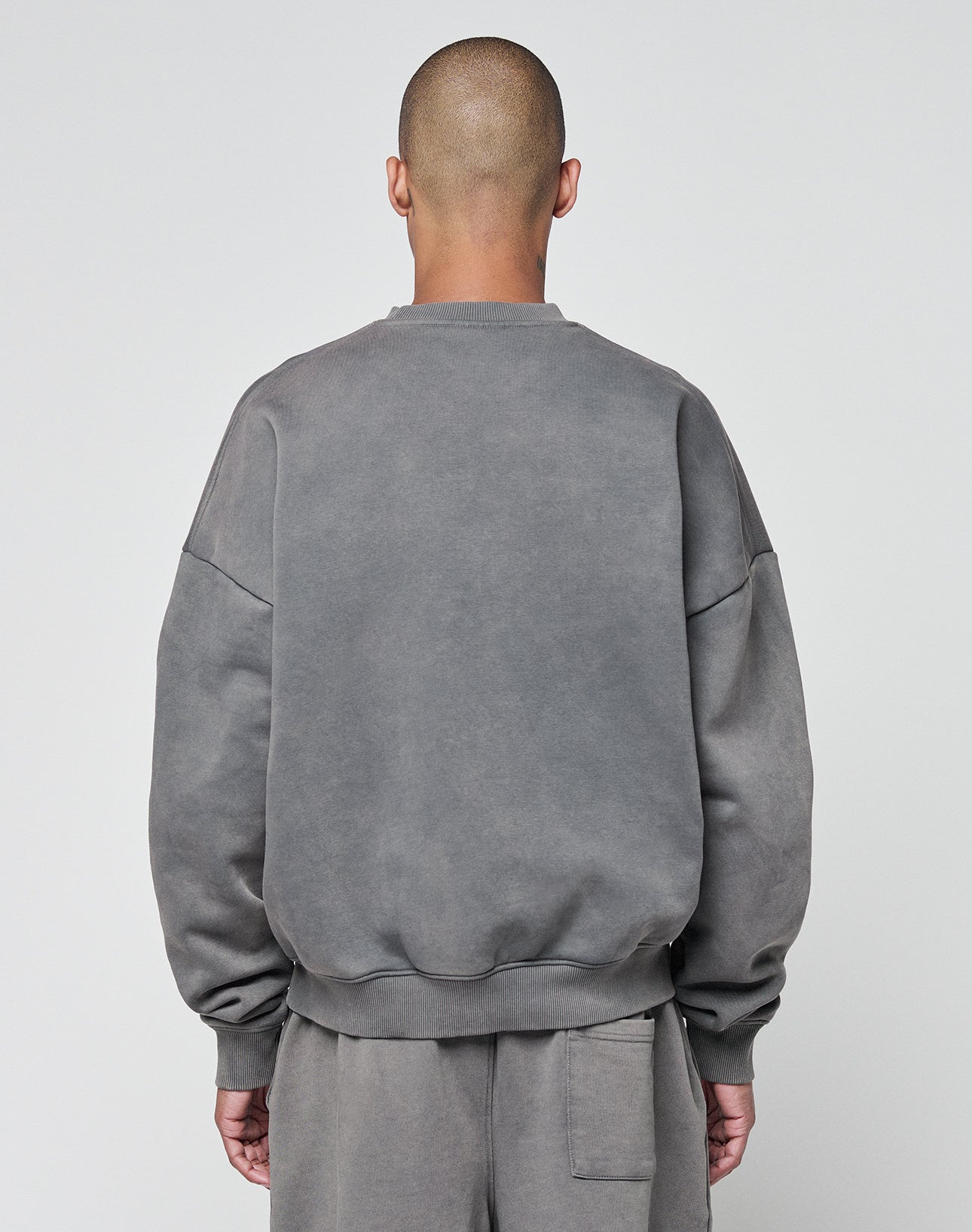 A person with a shaved head faces away from the camera, wearing the LIVE FAST DIE YOUNG Basic Chest Sweater in an oversize fit and matching faded gray sweatpants, made of soft cotton, set against a plain light background.