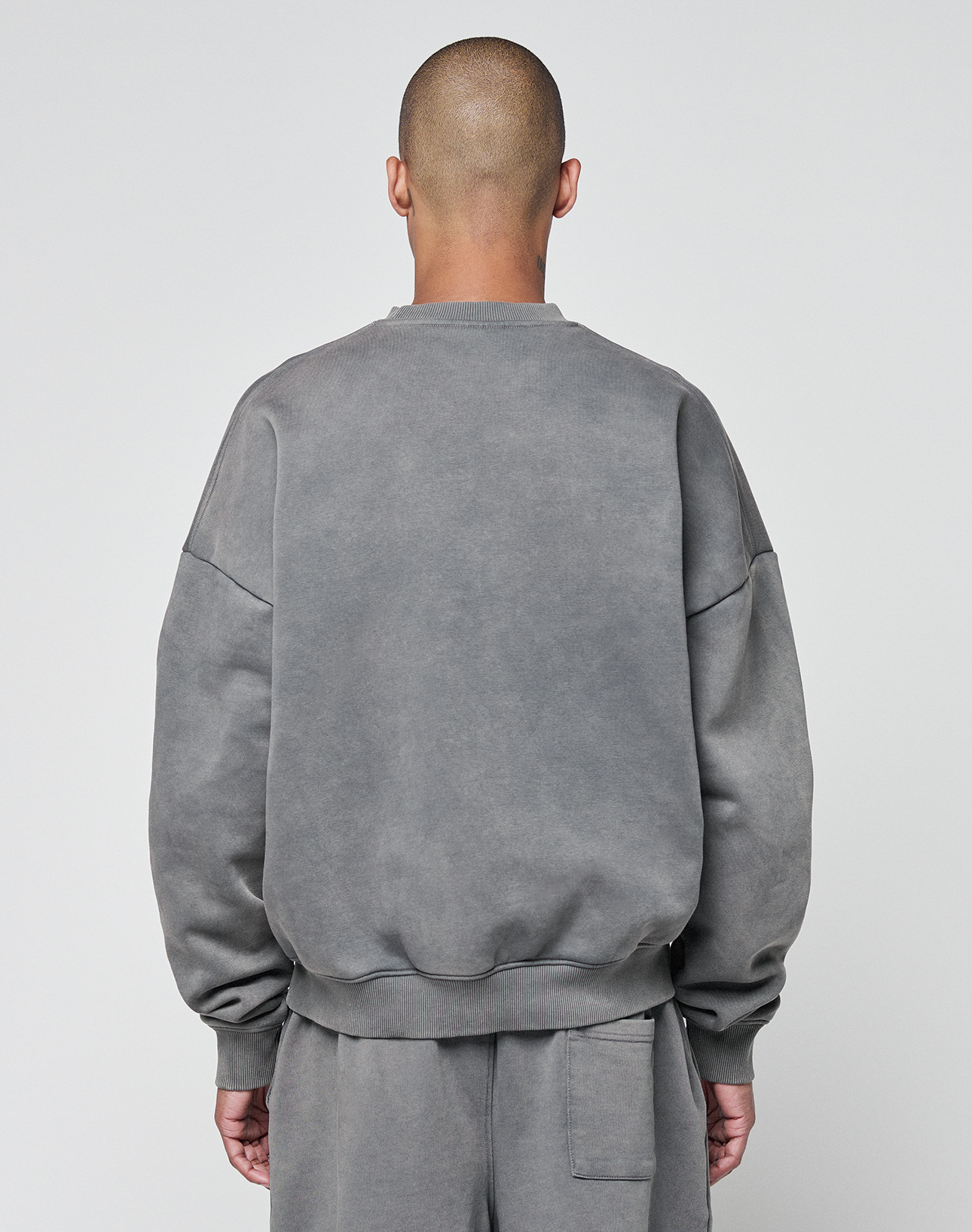 A person with a shaved head stands with their back to the camera, wearing a grey Basic Chest Sweater from LIVE FAST DIE YOUNG and matching sweatpants against a plain light background.