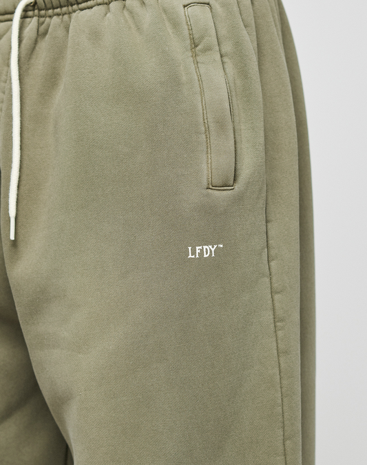 Close-up of the LIVE FAST DIE YOUNG Basic Wide Jogger in olive green, featuring a wide fit, elastic waistband, cream drawstring, slanted pocket, and a small white LFDY logo embroidered on the upper thigh.